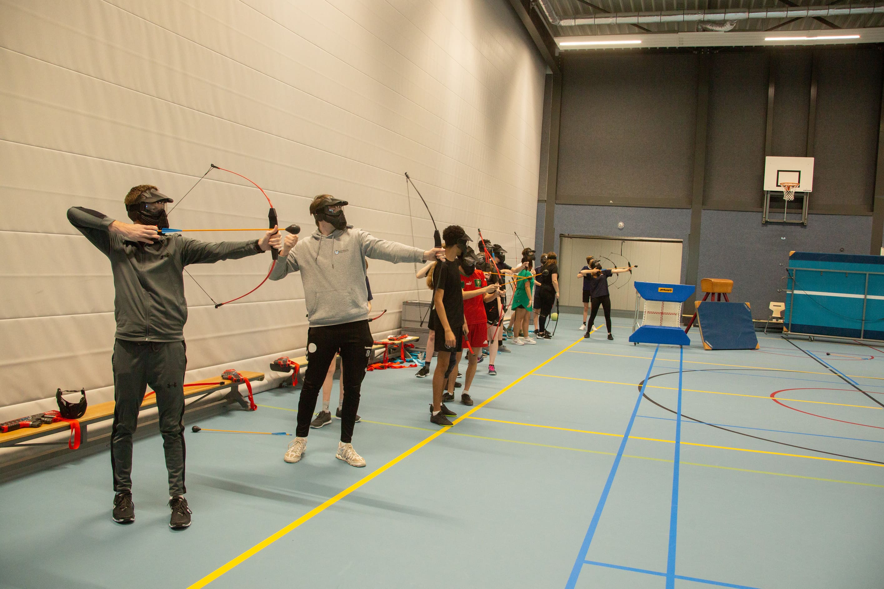 Spelers met een masker en boog spelen indoor archery tag in een gymzaal